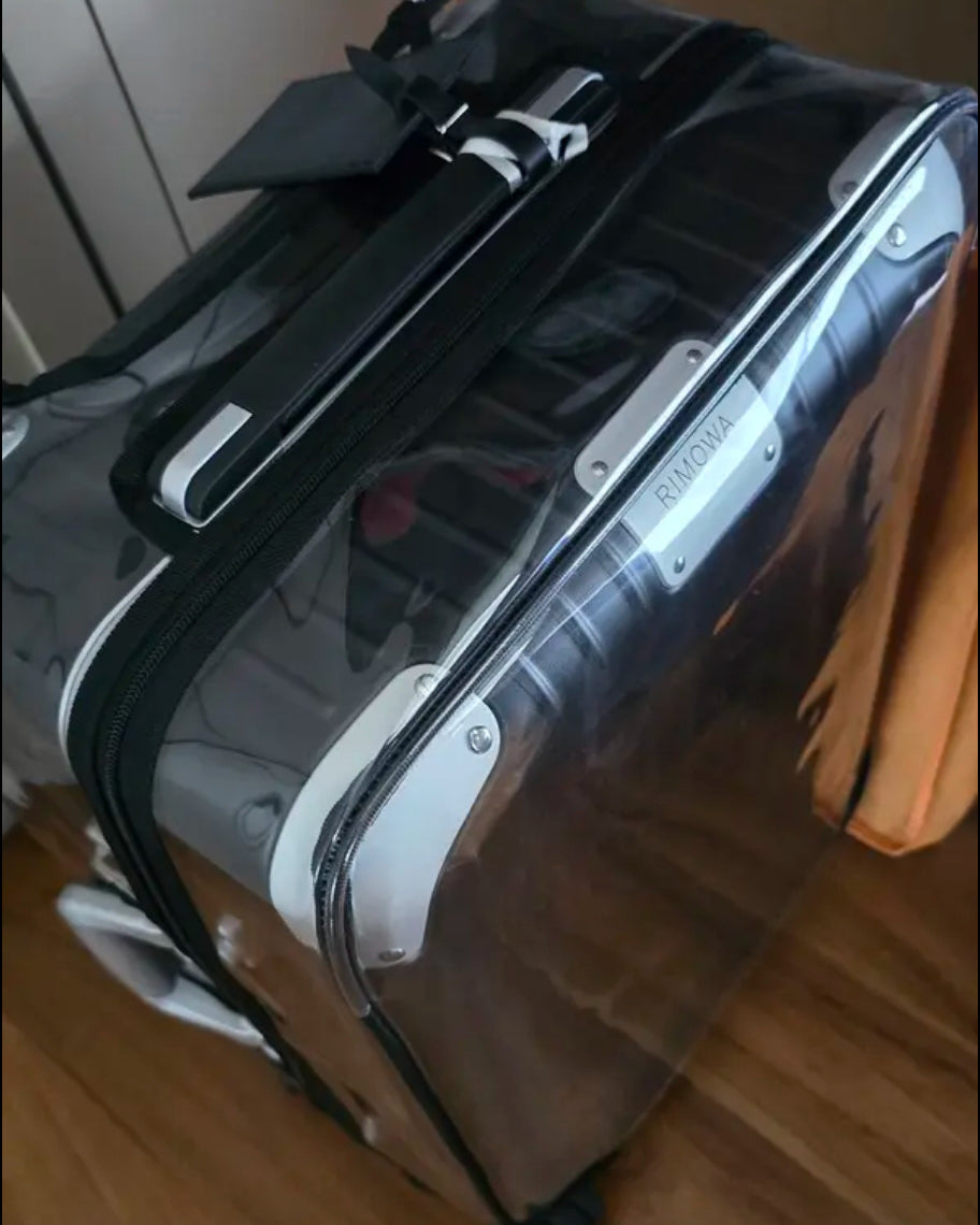 Close-up of a Rimowa Hybrid Check-In L in a clear Fixmeuniva cover with black trim, showing the top handle and silver corner protectors.