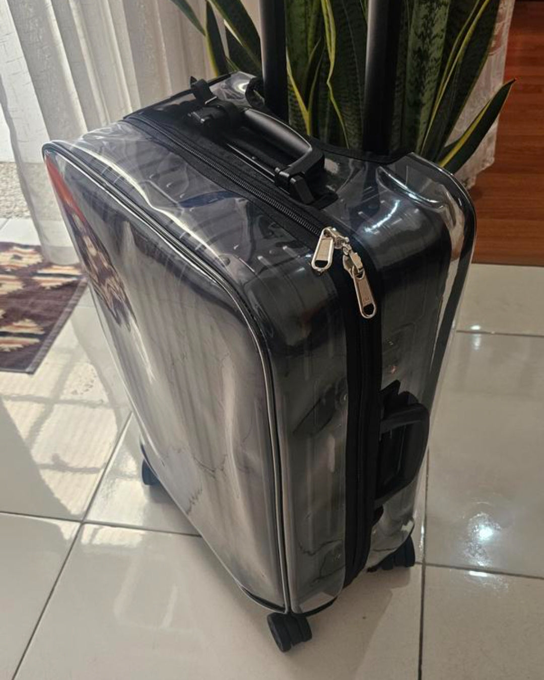 Rimowa Essential Check-In M in a clear Fixmeuniva cover with black trim, showing the top handle and ykk zipper