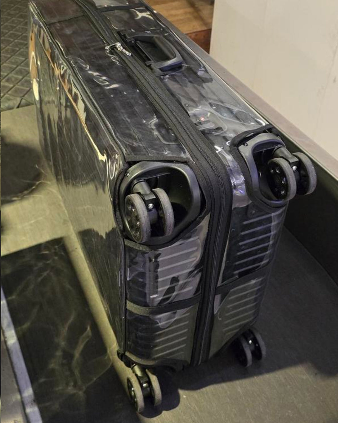 Close-up of a suitcase with a clear protective cover, showing its wheels and zipper.