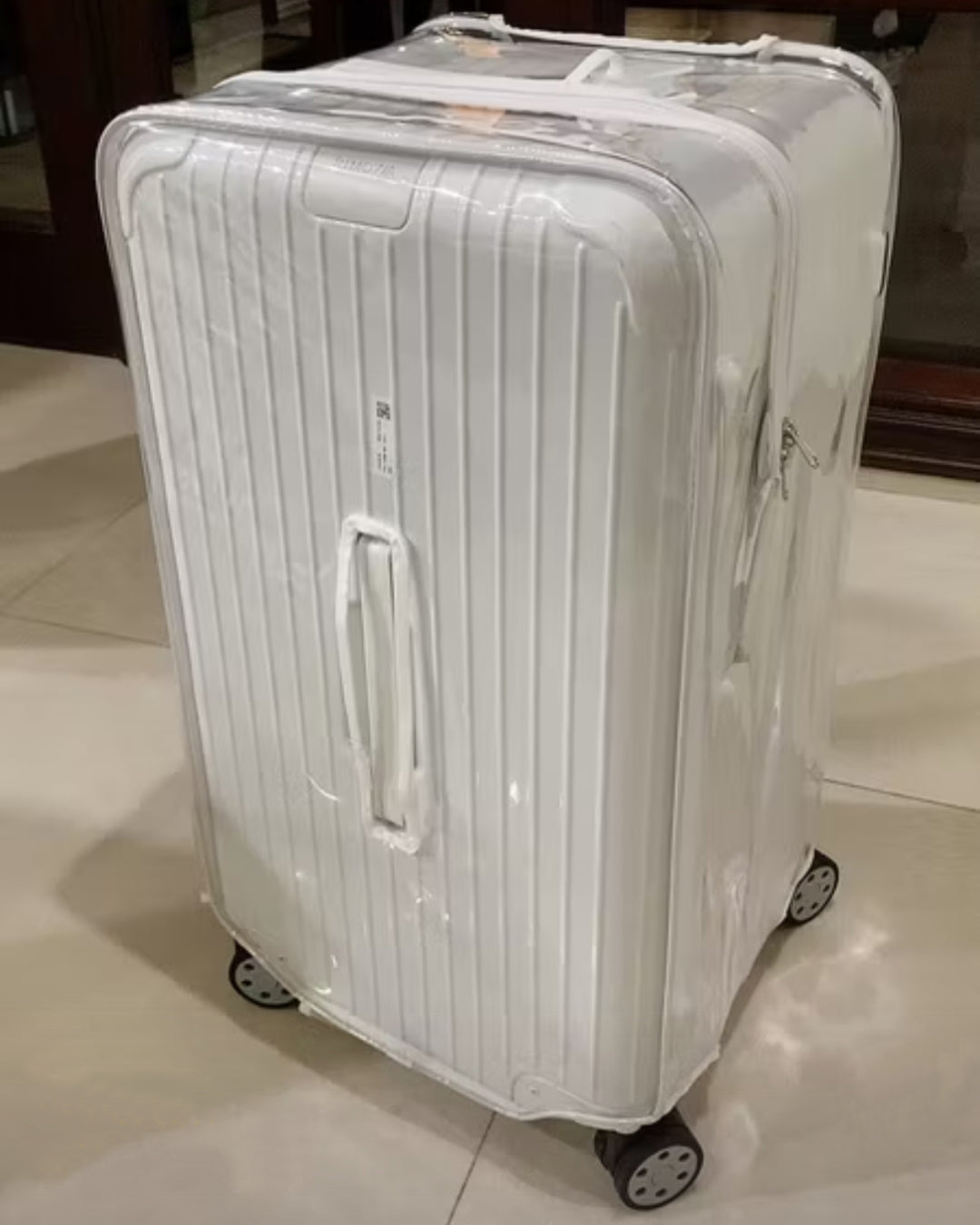 White Rimowa suitcase fitted with a clear luggage cover with white trim